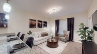 This single-floor residence offers a thoughtfully designed layout that balances comfort and functionality across its key living spaces. The living room serves as the heart of the home, featuring plush carpeting, a large window with blackout drapes that allow for adjustable natural light, and a track lighting fixture overhead. The space is well-proportioned, providing room for a full sofa arrangement centered around a round wooden coffee table and an accent armchair. The kitchen is a standout feature, showcasing rich dark mahogany cabinetry paired with light granite countertops, hardwood-style flooring, and black appliances including a refrigerator, electric range, and built-in microwave. A pendant light adds a refined touch above the counter workspace. The bedroom is a serene retreat with soft carpeting, a ceiling fan, a window dressed with sheer curtains for natural light, and built-in closet shelving for organized storage. A carpeted hallway connects the main areas, with additional shelving for convenience. The bathroom continues the design consistency of the home with matching dark cabinetry, granite countertops, hardwood-style flooring, and a tiled tub-shower combination, completing this cohesive and comfortable living space.