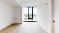 Located in the heart of Wilmington, DE, this two-bedroom, one-bathroom residence offers a thoughtfully designed, modern living environment with clean lines and a bright, minimalist aesthetic. Light wood flooring runs throughout the space, complementing the crisp white walls and creating a warm yet contemporary atmosphere.

The open-concept kitchen and living area serves as the central hub of the home. The kitchen features a peninsula with a white countertop and undermount sink, warm wood cabinetry, stainless steel appliances, and modern pendant lighting — all flowing seamlessly into the living area. Floor-to-ceiling windows in the living room flood the space with natural light and frame sweeping elevated views of the Wilmington cityscape and surrounding neighborhoods.

Both bedrooms continue the clean, modern design language, with large windows offering additional city views. The primary bedroom includes a sliding-door closet with built-in shelving for ample storage. The full bathroom is elegantly appointed with large-format marble-style tile in the tub surround, a wood vanity with white countertop, a rounded mirror with contemporary lighting, and neutral floor tile. The entryway provides a welcoming transition into the home, with convenient access to the kitchen and living spaces.