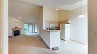 This single-floor residence offers a thoughtfully designed layout with a welcoming open-concept living and dining area at its heart. The living room is defined by dramatic vaulted ceilings that lend a sense of spaciousness, complemented by soft carpeting and a tile-surround fireplace that serves as a natural focal point. A pendant light fixture adds warmth to the space, while a sliding glass door allows natural light to pour in and provides access to an outdoor balcony.

The kitchen features light wood cabinetry, a peninsula breakfast bar, and a full suite of white appliances including a refrigerator, electric range with over-the-range microwave, and dishwasher — offering both practicality and efficiency.

The bedrooms are carpeted and generously proportioned, with select rooms benefiting from vaulted ceilings and multiple windows that frame lush green outdoor views. The bathrooms are finished with light tile flooring and light wood vanity cabinetry; one includes a shower-tub combination, and another features a well-lit vanity with mirror. A dedicated in-unit laundry room houses a full-size washer and dryer with built-in shelving above. Throughout, the residence maintains a clean, neutral palette creating a bright and adaptable living environment.