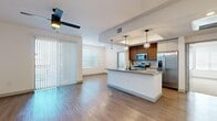 This single-story, 2-bedroom, 3-bathroom residence offers a thoughtfully designed open-concept layout finished with contemporary details throughout. The combined kitchen and living area serves as the heart of the home, featuring warm wood-look flooring, a ceiling fan, and generous natural light from large windows with vertical blinds and a sliding glass door that opens to the outdoors. The kitchen is appointed with stainless steel appliances including a gas range, microwave, and refrigerator, complemented by warm wood cabinetry, subway tile backsplash, and a central island with a grey quartz-style countertop, undermount sink, and matte black faucet. A tray ceiling with globe pendant lights adds architectural interest above the island. The bedrooms are carpeted and receive natural light through window blinds, with at least one bedroom featuring access to a dedicated walk-in closet with built-in shelving. The bathrooms echo the modern aesthetic with wood-toned vanities, grey countertops, undermount sinks, and backlit mirrors. A dedicated laundry room houses a full-size top-load washer and dryer with overhead shelving, adding everyday convenience to this well-equipped residence.