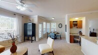 Located at 1310 Silver Sage Dr in Raleigh, NC, this single-floor residence offers a thoughtfully designed layout with comfortable living spaces throughout. The living room is bright and welcoming, featuring a ceiling fan, crown molding, plush carpeting, and a large window that invites abundant natural light and views of the surrounding greenery. Adjacent to the living area, the dining space is a standout feature, set within a bay window alcove with direct access to an outdoor balcony through a glass-paneled door — ideal for enjoying the outdoors. The kitchen is efficiently designed in a galley style, equipped with stainless steel appliances including a refrigerator, range, and microwave, complemented by warm wood cabinetry and granite-style countertops over tile flooring. A dedicated laundry room with full-size washer and dryer units adds everyday convenience. The bedroom is generously proportioned, finished with soft carpet, bright windows dressed with sheer curtains and blinds, and ample closet space. The bathroom is well-appointed with a granite-topped vanity, a large mirror, and a tub-shower combination with tile surround. Crown molding and a neutral color palette are consistent throughout, lending the space a cohesive and polished ambiance.