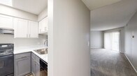 Located at 5771 Stone Mill Dr in Winston-Salem, NC, this single-floor 1-bedroom, 1-bathroom unit offers a practical and comfortable layout designed for everyday living. The open-concept kitchen and living area form the heart of the space, where the kitchen stands out with two-tone cabinetry — crisp white upper cabinets paired with gray lower cabinets — complemented by marble-look countertops, a stainless steel sink, and black appliances including a refrigerator and electric range. Wood-look flooring anchors the kitchen, transitioning seamlessly into the carpeted living room. The living room is spacious and bright, featuring neutral gray walls, a textured ceiling, and a sliding glass door fitted with vertical blinds that opens to a private balcony with outdoor views. The generously sized bedroom features plush carpet, neutral tones, and a window that allows natural light to filter in. The bathroom is clean and functional, offering a full-size soaking tub with shower, set against light wood-look tile flooring. A hallway connects the main areas of the unit, providing access to additional closet space. The overall aesthetic is modern and neutral, creating a move-in ready environment throughout.