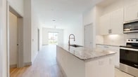 This 2-bedroom, 1-bathroom unit offers a clean, modern design with an open-concept layout that seamlessly connects the kitchen, dining, and living areas. Light wood-style flooring runs throughout the main living spaces, enhancing the bright and airy atmosphere created by the crisp white walls and abundant natural light.

The kitchen is well-appointed with white shaker cabinetry, granite countertops, a subway tile backsplash, and a full suite of stainless steel appliances including a refrigerator, range, and microwave. A large kitchen island with an undermount sink and additional seating space serves as the centerpiece of the open living area. The living room features a ceiling fan and a sliding glass door that opens to an outdoor balcony with green views.

The primary bedroom is generously sized with plush carpeting, a ceiling fan, and direct access to both a full bathroom and a walk-in closet outfitted with dual hanging rods and shelving. The second bedroom also features soft carpeting and two windows that bring in natural light. The shared bathroom includes a granite-topped white vanity, light wood-style flooring, a large mirror, and a tiled shower-tub combination. A dedicated closet provides additional storage within the unit.