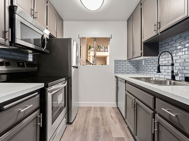 White tiled kitchen with stainless steel oven, microwave, and fridge.. - Riverbridge Apartments