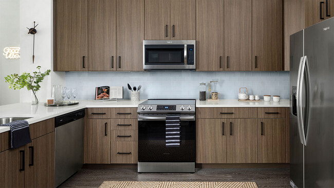 Cocina del apartamento con electrodomésticos de acero inoxidable, encimera de cuarzo y piso de madera. - Griffis Cherry Creek North