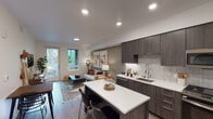 This thoughtfully designed one-bedroom residence offers a seamless open-concept floor plan that connects the kitchen, dining, and living areas into a cohesive and functional living space. The kitchen is a standout feature, boasting dark wood-grain cabinetry that extends to the ceiling, crisp white quartz countertops, under-cabinet lighting, a subway-style tile backsplash, and a full suite of stainless steel appliances including a gas range, built-in microwave, dishwasher, and French door refrigerator. A central island with bar seating provides additional prep space and a casual dining option. The open living and dining area is bathed in natural light from a glass door that leads to a private outdoor balcony, offering views of surrounding greenery. The living area features warm-toned accent walls and recessed lighting throughout. The bedroom is generously sized with a large window framing lush outdoor views, creating a tranquil retreat. Wood-look flooring runs consistently throughout the residence, tying the spaces together. The bathroom features dark wood vanity cabinetry, a backlit mirror, and a contrasting dark accent wall, lending a modern, spa-like quality to the space.