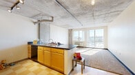 Located in Denver's vibrant Five Points neighborhood, this two-bedroom, one-bathroom unit offers an industrial-modern aesthetic defined by its signature exposed concrete ceilings and structural columns. The open-concept living and kitchen area forms the heart of the space, where a peninsula kitchen with dark countertops, warm maple cabinetry, stainless steel appliances, and a classic checkered tile floor transitions seamlessly into a carpeted living area. Large floor-to-ceiling windows flood the living room with natural light and frame sweeping views of the Denver skyline, creating a bright and airy atmosphere. Both bedrooms continue the industrial design language with exposed concrete ceilings, plush carpet flooring, and generous windows that capture city views. The primary bedroom includes a dedicated closet, while the second bedroom also features a reach-in closet for added storage. A separate walk-in closet provides additional organization space. The full bathroom offers a clean, functional layout complete with a tub-shower combination. Track lighting and industrial-style fixtures throughout reinforce the building's urban character, making this a compelling space in the heart of Denver.
