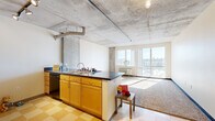 Located in Denver's vibrant Five Points neighborhood, this two-bedroom, one-bathroom unit offers an industrial-modern aesthetic defined by its signature exposed concrete ceilings and structural columns. The open-concept living and kitchen area forms the heart of the space, where a peninsula kitchen with dark countertops, warm maple cabinetry, stainless steel appliances, and a classic checkered tile floor transitions seamlessly into a carpeted living area. Large floor-to-ceiling windows flood the living room with natural light and frame sweeping views of the Denver skyline, creating a bright and airy atmosphere. Both bedrooms continue the industrial design language with exposed concrete ceilings, plush carpet flooring, and generous windows that capture city views. The primary bedroom includes a dedicated closet, while the second bedroom also features a reach-in closet for added storage. A separate walk-in closet provides additional organization space. The full bathroom offers a clean, functional layout complete with a tub-shower combination. Track lighting and industrial-style fixtures throughout reinforce the building's urban character, making this a compelling space in the heart of Denver.