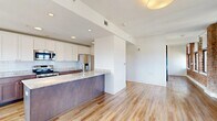 Located at 112 W Adams St in the heart of downtown Jacksonville, Florida, this single-floor residence blends historic architectural character with modern interior finishes. Exposed red brick walls are a defining feature throughout the living areas, lending an industrial-chic aesthetic that pays homage to the building's heritage. Large windows line the perimeter, flooding the space with natural light and framing sweeping elevated views of the Jacksonville skyline and surrounding cityscape.

Light hardwood-style flooring runs continuously throughout, complementing the warmth of the brick and the clean white of the walls and ceilings. The kitchen is thoughtfully designed with two-tone cabinetry—white upper cabinets paired with rich wood-toned lower cabinets—granite countertops, a white subway tile backsplash, and a full suite of stainless steel appliances. A central island with a built-in sink provides additional prep space and casual seating.

A hallway connects the main living area to the private quarters, featuring shaker-style doors with matte black hardware and a louvered closet door for ventilation. The walk-in closet offers generous storage with wraparound wire shelving. The bathroom is outfitted with accessibility features, including grab bars and a fold-down shower bench, finished with light tile flooring and coordinating cabinetry.