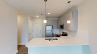 This thoughtfully designed 1-bedroom, 1-bathroom residence offers a clean, modern aesthetic across a single floor. The open-concept kitchen serves as the centerpiece of the living space, featuring an expansive quartz island with an undermount sink, crisp white subway tile backsplash, and sleek gray cabinetry with brushed metal hardware. Stainless steel appliances, including a full-size refrigerator, electric range, and built-in microwave, provide both style and functionality. Pendant lighting with frosted glass shades hangs above the island, adding warm, focused illumination to the kitchen workspace. Recessed lighting throughout ensures the space remains bright and welcoming. The wood-look flooring grounds the open layout with warmth and continuity, complementing the neutral color palette found throughout the residence. A dedicated entryway with a coat closet offers practical storage just inside the front door. The overall ambiance is fresh and contemporary, with attention to detail in the finishes that creates a polished, move-in-ready living environment well-suited for comfortable everyday living.