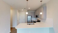 This thoughtfully designed 1-bedroom, 1-bathroom residence offers a clean, modern aesthetic across a single floor. The open-concept kitchen serves as the centerpiece of the living space, featuring an expansive quartz island with an undermount sink, crisp white subway tile backsplash, and sleek gray cabinetry with brushed metal hardware. Stainless steel appliances, including a full-size refrigerator, electric range, and built-in microwave, provide both style and functionality. Pendant lighting with frosted glass shades hangs above the island, adding warm, focused illumination to the kitchen workspace. Recessed lighting throughout ensures the space remains bright and welcoming. The wood-look flooring grounds the open layout with warmth and continuity, complementing the neutral color palette found throughout the residence. A dedicated entryway with a coat closet offers practical storage just inside the front door. The overall ambiance is fresh and contemporary, with attention to detail in the finishes that creates a polished, move-in-ready living environment well-suited for comfortable everyday living.