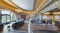 Located at 2300 N Lincoln Park West in Chicago's Lincoln Park neighborhood, this architecturally distinguished space showcases an exceptional blend of historic grandeur and contemporary design. The main hall commands attention with its soaring gilded ceilings adorned with intricate plasterwork, elaborate gold-leaf moldings, and richly detailed cornice work that speak to a Beaux-Arts heritage. Marble columns and stone pilasters frame the room, while ornate wrought-iron railings with scrollwork motifs define an interior balcony level that overlooks the expansive main floor below. A grand chandelier anchors the central hall, complementing the ambient warmth of the gold-toned ceiling. Large arched windows flood the space with natural light and offer views of the surrounding greenery of Lincoln Park. Seating areas are thoughtfully arranged throughout, featuring plush sofas, curved lounge chairs, and patterned striped carpeting that balance the classical architecture with modern comfort. A separate lounge area offers a more intimate setting with contemporary banquette seating, pendant lighting, and refined finishes. An adjacent room provides a serene retreat with neutral tones and clean-lined furnishings, contrasting elegantly with the ornate grandeur of the primary hall. Together, these spaces create a sophisticated and historically rich environment.