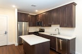 Located at 508 Washington Ave in Dumont, NJ, this single-floor unit offers a thoughtfully designed layout with a clean, contemporary aesthetic throughout. The open-concept living and kitchen area is anchored by rich, dark hardwood flooring that extends seamlessly through the main living spaces, complemented by crisp white walls and recessed lighting that create a bright, welcoming atmosphere.

The kitchen is a standout feature, showcasing dark espresso-toned shaker-style cabinetry that extends to the ceiling for ample storage. Light quartz countertops provide a striking contrast, while a center island offers additional prep and dining space. A full suite of stainless steel appliances—including a refrigerator, gas range, microwave, and dishwasher—adds a polished, functional touch.

The living area is generously proportioned with large windows that invite natural light and offer outdoor views of surrounding greenery. A separate carpeted room features sliding glass doors that open to an exterior view, providing a comfortable and private retreat.

The bathroom is finished with light neutral tile flooring and wall surround, featuring a full soaking tub with shower, toilet, and clean white fixtures. The overall design balances modern finishes with a warm, livable ambiance.