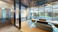 Located at 156 W Ocean Blvd in Long Beach, California, this single-floor commercial office space delivers a dynamic, design-forward environment tailored for creative work. The layout is organized around a central corridor finished with distinctive herringbone-patterned carpet tile, connecting a series of glass-walled private offices and conference rooms. Floor-to-ceiling curtain-wall glazing lines the perimeter, flooding the interior with natural light and offering views of the surrounding streetscape and greenery.

The space features a bold color palette, with accent walls in orange, red, teal, and green — including a striking living moss wall — punctuated by industrial-style ceiling treatments with exposed slatted metal detailing. Typographic signage, including phrases like "Space to Create," reinforces the creative identity of the environment.

A dedicated break area includes built-in cabinetry, a sink, and casual seating alongside large windows. A lounge area offers a built-in banquette with colorful cushions and low wooden accent tables, ideal for informal gatherings. An open seating nook with a round yellow bistro table provides an additional informal work or meeting spot. Decorative metal mesh partitions add visual texture throughout, contributing to the space's layered, urban-industrial aesthetic.