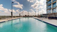 Located at 215 N Pine Street in the heart of uptown Charlotte, NC, this rooftop amenity deck offers a well-appointed outdoor retreat with sweeping views of the city skyline. The centerpiece of the space is a generously sized swimming pool with clear blue water, framed by wide concrete pool decking that provides ample room for lounging and socializing. Tall light poles line the perimeter, making the area functional well into the evening hours.

The deck is thoughtfully furnished with a variety of seating options to suit different preferences. Woven dome-style cabana pods with plush navy cushions offer cozy, semi-private nooks for relaxation, while traditional chaise lounges are arranged throughout the deck for open-air sunbathing. A dedicated shaded lounge area features a modern pergola structure with slatted wood privacy panels, providing a stylish retreat from direct sun.

The elevated position of the deck showcases panoramic views of Charlotte's urban skyline, with the glass-and-steel towers of uptown visible in the backdrop. The overall ambiance is modern and resort-inspired, blending clean architectural lines with comfortable, curated furnishings — creating an inviting urban oasis above the city.