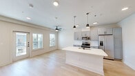 Located at 5545 Sofia Pl in Round Rock, TX, this single-floor unit offers a thoughtfully designed open-concept layout that maximizes every square foot. The living area features light-toned hardwood-style flooring and recessed lighting, creating a bright and airy atmosphere. A ceiling fan adds comfort to the spacious main living zone, which is bathed in natural light from multiple windows overlooking the surrounding exterior. A sliding glass door further enhances the connection to the outdoors. The kitchen is a standout feature, anchored by a large white-topped island with an undermount sink and matte black faucet, illuminated by a trio of modern pendant lights. Gray shaker-style cabinetry lines the walls alongside a classic white subway tile backsplash. Stainless steel appliances — including a refrigerator with ice maker, electric range, microwave, and dishwasher — complete the functional and stylish cooking space. The bathroom is clean and minimalist, outfitted with matte black hardware, a vanity with gray cabinetry, and a full tub-shower combination. A dedicated entry area with a front door and closet storage adds to the unit's practical layout, making this a well-rounded and modern living space.