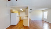 Located at 700 Stonehouse Dr in Napa, CA, this one-bedroom, one-bathroom residence offers a well-organized single-level layout with a variety of notable architectural and interior features. The open living room is a standout space, characterized by soaring vaulted ceilings, a ceiling fan, and gleaming hardwood floors that reflect natural light streaming in through windows overlooking an outdoor balcony. The textured ceiling adds visual interest, while a door provides direct access to the balcony, extending the living area outdoors. The kitchen is efficiently laid out in a galley style, featuring light wood cabinetry with brushed hardware, ample counter space, and white appliances including a range and refrigerator. It connects seamlessly to the living area via a partial wall with a pass-through design. The bedroom is a generously sized, carpeted retreat featuring a sliding glass door that opens to an outdoor space, providing both natural light and ventilation, along with a dedicated closet for storage. The bathroom includes warm wood-toned cabinetry beneath a wide vanity mirror illuminated by a row of lights, complemented by hardwood-style flooring. Throughout the residence, a neutral color palette and clean finishes create a bright, cohesive atmosphere well-suited for comfortable everyday living in the heart of Napa wine country.