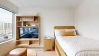 Located on Stokes Boulevard in Cleveland's vibrant University Circle neighborhood, this thoughtfully designed one-bedroom, one-bathroom unit maximizes every square foot with a clean, modern aesthetic. Light wood flooring runs throughout, complementing a bright, neutral color palette that creates an open and airy feel.

The bedroom offers a cozy yet functional retreat, featuring built-in storage drawers beneath the bed frame and a warm wood shelving unit that doubles as a media center — keeping the space organized and efficient. A dedicated closet with built-in shelving provides additional storage.

The kitchen is outfitted with white cabinetry, a light quartz countertop, stainless steel appliances including a full-size refrigerator, a microwave, and a cooktop with ventilation hood. A stacked washer and dryer unit is conveniently tucked within the unit, adding in-home laundry functionality.

The bathroom features a white vanity with a stone-toned countertop, undermount sink, matte black hardware accents, and a large mirror, contributing to a clean, contemporary finish. Large windows in the main living area allow ample natural light to fill the space, enhancing the overall brightness and welcoming ambiance of this efficiently designed home.