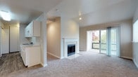 This single-floor residence offers a thoughtfully designed layout with a neutral color palette and practical finishes throughout. The living area serves as the focal point of the home, featuring a white tile-surround fireplace, vaulted ceilings with recessed lighting, and plush carpeting underfoot. A sliding glass door opens directly to a private balcony, framing views of surrounding greenery and inviting natural light deep into the space.

Adjacent to the living area, the galley-style kitchen is outfitted with white cabinetry, ample counter space, wood-look vinyl flooring, and white appliances including a range and refrigerator. A pass-through area connects the kitchen to the main living space for ease of circulation.

The bedrooms are generously proportioned, each finished with soft carpet and windows that allow natural light to filter in. Baseboard heating units are present in several rooms. One bedroom features an en-suite connection to a bathroom equipped with dual sinks, a speckled composite countertop, white cabinetry, and a tub-shower combination. A second bathroom mirrors similar finishes with a single-sink vanity and a clean, functional design. An open upper-level landing area with a decorative pendant light and staircase railing adds architectural interest to the overall layout.