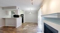 This single-story, 1-bedroom, 1-bathroom unit offers a thoughtfully designed layout that maximizes its compact footprint. The open-concept living and dining area features warm wood-look flooring, a textured ceiling, and large windows dressed with sheer vertical blinds that allow generous natural light to fill the space. A classic fireplace with a white mantle serves as a focal point in the living area, adding a cozy architectural detail.

The kitchen is efficiently laid out with white cabinetry, a light stone-finish countertop, and black appliances including a refrigerator, range, and microwave. A peninsula breakfast bar separates the kitchen from the living area, creating an open, connected feel. An in-unit washer and dryer are also accommodated within the kitchen space.

The bedroom is a comfortable, carpeted retreat featuring a ceiling fan with a light fixture and a walk-in closet equipped with built-in shelving — providing practical storage solutions. A window with blinds allows for natural light while maintaining privacy.

The bathroom is clean and functional, featuring a white vanity with storage, a light countertop, a combination tub and shower with tiled surround, and wood-look flooring that ties the space together with the rest of the unit.