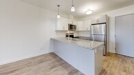 Located at 728 Meaford Ave in Langford, BC, this well-appointed one-bedroom, one-bathroom unit offers a functional and modern layout across a single floor. The open-concept kitchen is a standout feature, showcasing crisp white cabinetry, granite countertops, a subway tile backsplash, and a full suite of stainless steel appliances including a refrigerator, electric range, and over-the-range microwave. A peninsula with pendant lighting provides additional prep space and a casual dining area, while light wood-look flooring ties the kitchen and living areas together seamlessly. The bedroom is a comfortable retreat, finished with plush carpeting and a large window that frames lush greenery, filling the room with natural light. A dedicated closet offers convenient built-in shelving and hanging space. The bathroom is thoughtfully finished with a granite-topped vanity, white cabinetry, wood-look tile flooring, and a full shower-tub combination. A separate laundry area accommodates a stacked Whirlpool washer and dryer unit, adding everyday convenience. Throughout the unit, clean white walls and consistent finishes create a bright, cohesive, and move-in-ready atmosphere.
