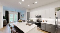 Located on North Tryon Street in Charlotte, NC, this thoughtfully designed 2-bedroom, 3-bathroom residence offers a well-appointed single-floor layout with a clean, contemporary aesthetic throughout. Warm hardwood-style flooring and crisp white walls create a cohesive backdrop across all rooms.

The kitchen is a standout feature, showcasing two-tone cabinetry in white and gray, stainless steel appliances including a French door refrigerator and electric range, and a generous island with seating — ideal for casual dining or entertaining. The open-concept design connects the kitchen seamlessly to the living area, which offers access to the outdoors through French doors and benefits from abundant natural light. A ceiling fan adds comfort to this inviting space.

The primary bedroom is well-sized, featuring large windows with outdoor views and direct access to an en-suite bathroom. The primary bath is finished with gray vanity cabinetry, white countertops, and a glass-enclosed shower, and opens into a spacious walk-in closet with extensive shelving and hanging storage. The second bedroom is equally bright, with large windows and access to its own bathroom, also finished with matching gray cabinetry and a tiled shower. A third bathroom provides additional convenience. Two dedicated closets ensure ample storage throughout the residence.