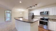 Located at 101 Sabal Palm Ln in Chesapeake, VA, this single-floor, 3-bedroom, 2-bathroom home offers a well-designed layout with a comfortable and functional living environment. The open-concept kitchen and living area serves as the heart of the home, featuring a curved granite-topped peninsula, white shaker-style cabinetry, stainless steel appliances including a refrigerator, range, and microwave, and hardwood flooring. Track lighting and recessed fixtures illuminate the kitchen, while a pendant light adds a focal point above the peninsula. The living area transitions seamlessly from the kitchen, finished with neutral carpet and wainscoting detail along the walls. Each of the three bedrooms is carpeted and fitted with a ceiling fan, offering a comfortable retreat. The primary bedroom is generously sized and includes a sliding glass door leading to a private outdoor deck with exterior views. The two bathrooms are finished consistently with dark granite countertops, white cabinetry, and hardwood flooring. One bathroom features a tiled tub-shower combination with a classic checkered tile accent border. Throughout the home, warm neutral tones and an abundance of natural light from multiple windows create a bright and welcoming ambiance.