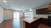 This single-story space is designed with an open-concept layout that seamlessly connects the kitchen and living area. The living room is generously sized, featuring rich hardwood-style flooring, recessed lighting, and abundant natural light streaming through a wide picture window and a sliding glass door fitted with vertical blinds, providing outdoor access and views.

The kitchen is well-appointed with dark espresso cabinetry extending to the ceiling for ample storage, granite-style countertops, black appliances including a range, microwave, and refrigerator, and a peninsula that doubles as a breakfast bar. A dedicated laundry closet with louvered doors is conveniently located adjacent to the kitchen.

Two bathrooms mirror each other in finish quality, each featuring dark espresso vanity cabinetry, marble-style countertops, a single undermount sink, and a large frameless mirror. One bathroom includes a walk-in shower, while the other offers a tub-shower combination.

The bedroom features plush carpet flooring, neutral-toned walls, and a window that allows natural light to filter in. Throughout the space, consistent neutral paint tones and cohesive finishes create a clean, unified aesthetic.