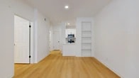 This well-appointed 1-bedroom, 1-bathroom unit offers a clean, modern aesthetic throughout its single-floor layout. Light wood flooring flows seamlessly across every room, complementing the crisp white walls and creating a bright, airy atmosphere. The open-concept living area is generously sized, featuring large windows that invite abundant natural light and a glass entry door that enhances the sense of openness. Built-in shelving adjacent to the living space provides functional display and storage options. The kitchen is thoughtfully designed with white shaker-style cabinetry, a herringbone tile backsplash, a peninsula with an integrated sink and matte black faucet, and a full suite of stainless steel appliances including a range, microwave, and refrigerator. A hallway connects the main living area to the private bedroom, which features a ceiling fan, a large window with natural views, and direct access to a dedicated walk-in closet equipped with wire shelving on multiple walls. The bathroom is finished to a high standard, showcasing large-format tile flooring, a white vanity with ample cabinetry and matte black hardware, a glass-enclosed tub-shower combination with marble-style tile surround, and a sleek mirror. The overall design is cohesive, functional, and move-in ready.