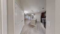 This well-appointed single-floor residence offers a thoughtfully designed open-concept layout that seamlessly connects the kitchen, dining, and living areas. The herringbone-patterned luxury vinyl flooring flows consistently throughout, lending a contemporary and cohesive aesthetic to the entire space.

The kitchen serves as the centerpiece of the home, showcasing rich dark espresso cabinetry, speckled granite countertops, and a full suite of stainless steel appliances including a refrigerator, range, and built-in microwave. A large kitchen island with an integrated sink and pendant lighting overhead provides both additional workspace and a natural gathering point. A classic tile backsplash adds a refined finishing touch.

The living area is bright and open, featuring a ceiling fan and a door leading to an exterior patio or entry point, allowing for natural light and convenient outdoor access. The neutral color palette throughout creates a calm, inviting ambiance.

The bedroom offers a generously sized layout with herringbone flooring, access to a walk-in closet with built-in shelving, and ample wall space for flexible furniture arrangement. The bathroom is clean and functional, featuring dark cabinetry with a white countertop vanity, a soaking tub with tiled surround, and an illuminated mirror. A large storage closet near the entry further enhances the practical appeal of this well-designed residence.