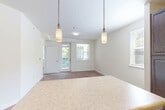 Located at 12330 Vivian Adams Dr in Waldorf, MD, this 2-bedroom, 1-bathroom single-floor home offers a well-organized layout across a comfortable footprint. The open-concept living area seamlessly connects the kitchen, dining, and living spaces, creating a bright and functional hub for daily life. The kitchen is appointed with rich, dark espresso cabinetry, black appliances including a range and refrigerator, light stone-look countertops, and a peninsula island with an overhang for casual seating. Stylish dual pendant lights illuminate the transition between the kitchen and living area, which features warm hardwood-style flooring throughout. The living room is bathed in natural light from multiple windows, with a door leading to a private outdoor balcony area. Both bedrooms are carpeted and well-proportioned, each receiving natural light through large windows with wooded views. The spacious primary bedroom includes direct access to the bathroom, which features dark wood cabinetry consistent with the kitchen's design aesthetic. Three closets throughout the home provide ample storage. A dedicated laundry area and a connecting hallway round out the practical and efficient floor plan of this Waldorf residence.