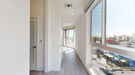 Located on Beverly Boulevard in Los Angeles, this modern 2-bedroom, 1-bathroom unit offers a bright, contemporary living experience across a single floor. The open-concept kitchen and living area is anchored by large floor-to-ceiling windows that flood the space with natural light and frame expansive city views. The kitchen is outfitted with warm wood cabinetry, white quartz countertops, a stainless steel sink, and a full suite of stainless steel appliances including a gas range, microwave, dishwasher, and refrigerator. Light wood-toned flooring runs throughout the entire unit, lending a clean, cohesive aesthetic. The primary bedroom is a well-proportioned retreat featuring a large window with outdoor views and access to a balcony. The second bedroom offers a bright, minimalist space with recessed lighting. Both bedrooms benefit from natural light and a calm, neutral palette. The hallways are lined with windows that continue to bring in sunlight and views of the surrounding cityscape. The bathroom features a full tub-shower combination with white subway tile surround, a vanity, and matching light flooring. The overall ambiance of the unit is clean, modern, and airy, reflecting a thoughtfully designed urban living space in the heart of Los Angeles.