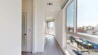 Located on Beverly Boulevard in Los Angeles, this modern 2-bedroom, 1-bathroom unit offers a bright, contemporary living experience across a single floor. The open-concept kitchen and living area is anchored by large floor-to-ceiling windows that flood the space with natural light and frame expansive city views. The kitchen is outfitted with warm wood cabinetry, white quartz countertops, a stainless steel sink, and a full suite of stainless steel appliances including a gas range, microwave, dishwasher, and refrigerator. Light wood-toned flooring runs throughout the entire unit, lending a clean, cohesive aesthetic. The primary bedroom is a well-proportioned retreat featuring a large window with outdoor views and access to a balcony. The second bedroom offers a bright, minimalist space with recessed lighting. Both bedrooms benefit from natural light and a calm, neutral palette. The hallways are lined with windows that continue to bring in sunlight and views of the surrounding cityscape. The bathroom features a full tub-shower combination with white subway tile surround, a vanity, and matching light flooring. The overall ambiance of the unit is clean, modern, and airy, reflecting a thoughtfully designed urban living space in the heart of Los Angeles.