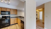Located at 1870 N Lennox St in Olathe, Kansas, this two-bedroom, two-bathroom residence offers a practical and comfortable single-floor layout. The open-concept living and kitchen area serves as the heart of the home, where wood-look flooring flows throughout. The living room is bathed in natural light from a sliding glass door that opens to an outdoor patio, fitted with vertical blinds and a textured ceiling overhead. The kitchen is well-equipped with light oak cabinetry, dark granite-style countertops, a full suite of black appliances including a refrigerator, range, microwave, and dishwasher, and a double-basin sink. Track lighting illuminates the space, and a peninsula counter provides a convenient pass-through. A stacked washer and dryer unit is conveniently located in a dedicated laundry area within the unit. Both bedrooms feature plush carpeting and ceiling fans, with the primary bedroom benefiting from a private en-suite bathroom and a walk-in closet. The second bedroom includes its own closet as well. Each bathroom is finished with wood-toned vanity cabinetry, dark countertops, and a tub-shower combination. A utility room and additional closets round out the functional storage throughout this well-appointed home.
