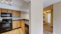 Located at 1870 N Lennox St in Olathe, Kansas, this two-bedroom, two-bathroom residence offers a practical and comfortable single-floor layout. The open-concept living and kitchen area serves as the heart of the home, where wood-look flooring flows throughout. The living room is bathed in natural light from a sliding glass door that opens to an outdoor patio, fitted with vertical blinds and a textured ceiling overhead. The kitchen is well-equipped with light oak cabinetry, dark granite-style countertops, a full suite of black appliances including a refrigerator, range, microwave, and dishwasher, and a double-basin sink. Track lighting illuminates the space, and a peninsula counter provides a convenient pass-through. A stacked washer and dryer unit is conveniently located in a dedicated laundry area within the unit. Both bedrooms feature plush carpeting and ceiling fans, with the primary bedroom benefiting from a private en-suite bathroom and a walk-in closet. The second bedroom includes its own closet as well. Each bathroom is finished with wood-toned vanity cabinetry, dark countertops, and a tub-shower combination. A utility room and additional closets round out the functional storage throughout this well-appointed home.