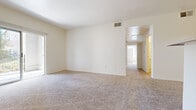 This single-floor unit features a neutral, move-in-ready interior with a practical and open layout. The main living area is generously proportioned, with plush beige carpeting, white walls, and a sliding door that invites natural light while providing outdoor access. A ceiling vent and multiple electrical outlets are conveniently positioned throughout the space.

The layout flows seamlessly into a dining area adjacent to the kitchen, which is outfitted with warm wood-toned cabinetry, a breakfast bar countertop, and standard appliances including a range. Tile flooring transitions from the kitchen into the connecting areas.

The bedrooms are carpeted and feature bright white walls with vaulted or elevated ceilings that enhance the sense of space. Each bedroom includes a closet with a hanging rod, and windows fitted with horizontal blinds provide natural light and privacy. One bedroom benefits from direct access to a bathroom.

The bathrooms feature tile flooring in a warm stone tone. One bathroom includes a full tub and shower combo with white tile surround, while another features dual wood-toned vanities flanking a centered window, offering generous counter and storage space. Both bathrooms are finished with white fixtures and well-lit vanity mirrors.