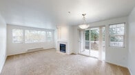 Located in Portland's 97229 zip code, this single-floor unit offers a well-organized layout with a bright, neutral aesthetic throughout. The spacious living room serves as the heart of the home, featuring a fireplace with a clean white surround, large windows that draw in natural light, and sliding glass doors opening onto a private balcony with views of surrounding greenery. Plush carpeting and a pendant light fixture complete the welcoming atmosphere.

The galley-style kitchen is efficiently designed with white cabinetry, laminate countertops, a full suite of white appliances including a dishwasher, range, microwave, and refrigerator, and a window overlooking the outdoors. Light hardwood-style flooring runs through the kitchen and connecting areas.

The bedrooms are carpeted and generously sized, each with windows providing natural light and baseboard heating. One bedroom offers a peaceful view of neighboring rooftops and trees.

The bathroom features a wide vanity with ample cabinet storage, a large mirror with overhead lighting, and a soaking tub with tiled surround. A dedicated laundry closet houses a full-size washer and dryer, adding everyday convenience to this well-appointed space.