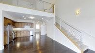 Located at 6800 Embarcadero Lane in Carlsbad, this Plan E unit offers a thoughtfully designed multi-story layout spread across three floors. The main living area immediately impresses with its soaring double-height ceilings, creating an expansive, airy atmosphere filled with a sense of openness and volume. Rich, dark hardwood flooring runs throughout the main level, providing a warm contrast to the crisp white walls and modern architectural details.

The open-concept kitchen is seamlessly integrated into the living space and features warm wood cabinetry, stone tile backsplash, a stainless steel dishwasher, and a sink positioned beneath a window that brings in natural light. Recessed lighting throughout the main level ensures the space remains bright and welcoming.

A striking staircase with sleek cable railing and natural wood handrails ascends from the main living area, leading to an upper-level loft or landing overlooking the floor below. The horizontal cable railing system adds a contemporary, industrial-chic touch that complements the clean, modern aesthetic of the home. With three full floors, the layout offers generous flexibility for living, working, and entertaining. This vacant unit presents a versatile and stylish residential opportunity in the desirable Carlsbad area.