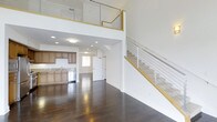 Located at 6800 Embarcadero Lane in Carlsbad, this Plan E unit offers a thoughtfully designed multi-story layout spread across three floors. The main living area immediately impresses with its soaring double-height ceilings, creating an expansive, airy atmosphere filled with a sense of openness and volume. Rich, dark hardwood flooring runs throughout the main level, providing a warm contrast to the crisp white walls and modern architectural details.

The open-concept kitchen is seamlessly integrated into the living space and features warm wood cabinetry, stone tile backsplash, a stainless steel dishwasher, and a sink positioned beneath a window that brings in natural light. Recessed lighting throughout the main level ensures the space remains bright and welcoming.

A striking staircase with sleek cable railing and natural wood handrails ascends from the main living area, leading to an upper-level loft or landing overlooking the floor below. The horizontal cable railing system adds a contemporary, industrial-chic touch that complements the clean, modern aesthetic of the home. With three full floors, the layout offers generous flexibility for living, working, and entertaining. This vacant unit presents a versatile and stylish residential opportunity in the desirable Carlsbad area.