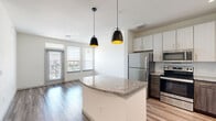 Located at 2301 Wallace Rd in Baytown, TX, this well-appointed one-bedroom, one-bathroom residence offers a thoughtfully designed single-floor layout. The open-concept kitchen and living area serves as the heart of the home, anchored by a granite-topped island illuminated by two stylish pendant lights. The kitchen features a two-tone cabinet design pairing white upper cabinets with dark lower cabinetry, a subway tile backsplash, and a full suite of stainless steel appliances including a refrigerator, electric range, microwave, and dishwasher. Wood-look flooring runs throughout the main living areas, complementing the bright, neutral color palette. The living room receives generous natural light through large windows with exterior views, and includes a dedicated entry door. The bedroom is carpeted for comfort, features a ceiling fan, and is served by two closets, one of which is a walk-in. Windows in the bedroom also offer outdoor views. The bathroom is well-appointed with a granite vanity, white cabinetry with gold hardware, wood-look flooring, and a full tub-shower combination with large-format tile surround. A dedicated in-unit laundry room with full-size washer and dryer hookups adds everyday convenience to this complete and functional residence.