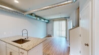 This 1-bedroom, 1-bathroom unit in Clawson, Michigan offers a thoughtfully designed layout that blends modern finishes with industrial character. Exposed silver ductwork runs through the open-concept kitchen and living area, adding a distinctive loft-like aesthetic to the space. The kitchen is well-appointed with white shaker cabinetry, granite countertops, a kitchen island with a built-in sink and gooseneck faucet, white appliances including an electric range, built-in microwave, refrigerator, and dishwasher, complemented by a subway tile backsplash. Light hardwood flooring extends throughout the kitchen and main living area, brightened by recessed lighting and a large sliding glass door with vertical blinds that invites natural light. The bedroom features plush carpeting, a window with blinds, and access to a dedicated closet space, offering a comfortable and private retreat. The bathroom is finished with a white vanity with storage drawers, a framed mirror, and hardwood-style flooring, maintaining a clean and cohesive look. Throughout the unit, neutral wall tones and clean white trim create a bright, welcoming ambiance suited for comfortable everyday living.