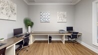 Located at 920 Stockbridge Dr. in Fort Mill, SC, this single-floor business center offers a clean, professional environment designed to meet everyday computing and productivity needs. The room is finished with warm, neutral gray walls accented by crisp white crown molding and baseboards, creating a polished and welcoming aesthetic throughout.

The centerpiece of the space is an L-shaped, granite-topped workstation that comfortably accommodates multiple users simultaneously. Several desktop computers with full keyboards and peripherals are positioned along the counter, along with a printer for added convenience. Ergonomic office chairs and padded seating ensure comfort during extended use.

The flooring consists of durable wood-look planks that add warmth to the space while maintaining a professional look. Natural light filters in through a large frosted glass window, complementing the overhead lighting and keeping the room bright without harsh glare. Glass-paneled interior doors with transom windows connect the business center to adjacent areas, maintaining an open sightline and encouraging a sense of connectivity throughout the facility.

Thoughtful decorative touches—including two framed canvas wall prints and a tall potted tropical plant—add a refined, inviting character to the space. The overall design balances functionality with comfort, making it an ideal setting for residents or guests seeking a dedicated workspace.