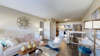 This single-floor residence offers a thoughtfully designed open-concept layout that seamlessly connects the living area and kitchen, creating a bright and cohesive living environment. The living room features rich hardwood-style flooring, large windows that invite abundant natural light, and a welcoming ambiance accented by warm neutral tones on the walls. A stylish entryway area provides additional flexible space, ideal for a home office or reading nook.

The kitchen is well-equipped with stainless steel appliances, including a refrigerator, range, and microwave, complemented by crisp white shaker-style cabinetry and a classic subway tile backsplash. Light-toned countertops add to the clean aesthetic, while a bar-height dining table with seating offers a casual dining option directly adjacent to the kitchen.

The bedroom is a tranquil retreat, carpeted for comfort and filled with natural light through well-sized windows dressed with blinds and curtains. It provides ample space for a full bedroom suite.

The bathroom is clean and functional, featuring hardwood-style flooring, a shower/tub combination, and neutral wall tones. Throughout the unit, consistent design choices — including warm neutrals, gold accents, and modern fixtures — contribute to a cohesive and inviting atmosphere.