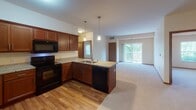 This single-floor residence on 156th Lane NW in Andover, Minnesota offers a well-designed, accessible layout suited for comfortable everyday living. The open-concept kitchen and living area forms the heart of the home, where rich cherry wood cabinetry, granite countertops, and black appliances — including a refrigerator, range, microwave, and dishwasher — combine for a functional yet attractive space. Hardwood-style flooring runs through the kitchen, transitioning to plush carpet in the expansive living area, which features a sliding glass door providing natural light and access to an outdoor balcony.

The bedrooms are carpeted and filled with natural light from windows overlooking greenery. One bedroom includes a ceiling fan, while the others offer ample space and neutral tones throughout. A wide hallway connects the rooms, with a closet providing convenient storage.

Both bathrooms are thoughtfully designed with accessibility in mind, featuring stainless steel grab bars, granite-topped vanities, and tile-style flooring. One bathroom includes a walk-in shower, while the other offers a full tub-shower combination. Warm neutral walls and recessed lighting carry throughout, creating a cohesive and welcoming ambiance across the entire unit.