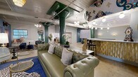 Located at 2400 Grayland Ave in Richmond, VA, this one-of-a-kind event and lounge space masterfully combines industrial architecture with vibrant, eclectic design. The single-floor layout offers a generous, open footprint anchored by striking green structural columns and exposed ductwork that celebrate the building's raw, industrial bones. Polished concrete floors extend throughout, providing a sleek and durable foundation that contrasts beautifully with the richly layered décor above.

The main lounge area features a tufted olive leather Chesterfield sofa, bold patterned rugs in deep blue, and an array of unique seating options including velvet chairs and animal-print ottomans. A curved bar with a decorative gold paneled front and marble countertop serves as a dramatic focal point, framed by elaborate hand-painted murals adorning the arched ceiling above. Tiered fringe chandeliers and globe pendant lights add warmth and theatrical ambiance throughout.

A more intimate dining area offers tufted pink booth seating set within curtained alcoves, providing a cozy counterpoint to the open main floor. An electric fireplace with a sleek tile surround anchors another lounge vignette nearby. The space also includes a corridor with additional seating nooks, wall sconces, and access to adjoining rooms, making it highly adaptable for private events, gatherings, or social venues.