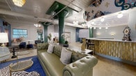 Located at 2400 Grayland Ave in Richmond, VA, this one-of-a-kind event and lounge space masterfully combines industrial architecture with vibrant, eclectic design. The single-floor layout offers a generous, open footprint anchored by striking green structural columns and exposed ductwork that celebrate the building's raw, industrial bones. Polished concrete floors extend throughout, providing a sleek and durable foundation that contrasts beautifully with the richly layered décor above.

The main lounge area features a tufted olive leather Chesterfield sofa, bold patterned rugs in deep blue, and an array of unique seating options including velvet chairs and animal-print ottomans. A curved bar with a decorative gold paneled front and marble countertop serves as a dramatic focal point, framed by elaborate hand-painted murals adorning the arched ceiling above. Tiered fringe chandeliers and globe pendant lights add warmth and theatrical ambiance throughout.

A more intimate dining area offers tufted pink booth seating set within curtained alcoves, providing a cozy counterpoint to the open main floor. An electric fireplace with a sleek tile surround anchors another lounge vignette nearby. The space also includes a corridor with additional seating nooks, wall sconces, and access to adjoining rooms, making it highly adaptable for private events, gatherings, or social venues.