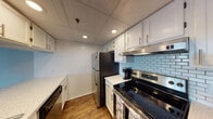 This single-floor unit offers a clean, modern aesthetic with thoughtful updates throughout. The open-concept living area is anchored by rich hardwood-style flooring and features a large window with vertical blinds, allowing generous natural light to fill the space. A ceiling fan adds both function and character to the living area, which flows seamlessly toward the kitchen via a convenient pass-through opening.

The kitchen is well-equipped and efficiently designed, featuring white cabinetry with brushed nickel hardware, light stone-look countertops, a stainless steel refrigerator, an electric range with a stainless range hood, a built-in dishwasher, and a stainless steel sink. A light blue subway tile backsplash provides a fresh, contemporary accent, and recessed lighting and a drop ceiling complete the look.

The bedroom area is carpeted for comfort and offers a generous layout with direct access to additional rooms, providing flexible use of space. A large window in the bedroom allows for ample natural light and exterior views. The bathroom includes a full tub and shower combination with clean white tile surround and brushed nickel fixtures. Throughout the unit, neutral tones and updated finishes create a cohesive, move-in ready environment.