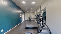 Located at 1901 E Apache Blvd in Tempe, Arizona, this fitness center is a dedicated exercise room designed to provide residents with essential workout amenities in a practical, well-organized space. The room features a bold teal accent wall that contrasts with neutral gray tones on the remaining walls and ceiling, creating a visually dynamic environment. Durable dark concrete flooring runs throughout, offering a sturdy surface well-suited for exercise equipment and high-traffic use. Recessed lighting illuminates the space evenly from a textured ceiling above.

The facility is equipped with a TM6000 treadmill and an elliptical trainer for cardiovascular workouts, alongside a multi-station cable strength training machine for resistance exercises. A large floor-to-ceiling mirror spans one wall, visually expanding the room and allowing users to monitor their form during workouts. A built-in dual water fountain and bottle-filling station is mounted along the teal wall, providing convenient hydration access. The space is accessed through a secured keypad entry door, with a second set of glass double doors offering a secondary exit to the outdoors, allowing natural light to filter into the room. The overall layout is efficient and functional, making the most of the available square footage for a complete workout experience.