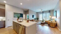 This well-appointed single-floor residence offers a thoughtfully designed open-concept layout that seamlessly connects the kitchen, dining, and living areas. The kitchen is a standout feature, showcasing a large center island with white quartz countertops, taupe cabinetry, stainless steel appliances — including a refrigerator, microwave, and range — and a subway tile backsplash. Bar seating at the island makes it ideal for casual dining and entertaining. Light wood-style flooring flows throughout the main living areas, enhancing the bright, airy atmosphere.

The living room is generously proportioned, with large windows and a glass door that invite abundant natural light and provide outdoor access. A ceiling fan adds comfort to the space. The unit includes two well-sized bedrooms, each featuring plush carpet flooring and ample natural light. Both bathrooms are finished with gray cabinetry, quartz countertops, and LED-backlit mirrors, with one bathroom offering a soaking tub with tiled surround. A dedicated walk-in closet is accessible from the primary bathroom. An in-unit washer and dryer closet adds everyday convenience. The overall design is modern and cohesive, with neutral tones and clean lines throughout.