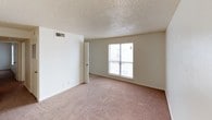 This single-floor residence offers a practical and functional layout with a clean, neutral aesthetic throughout. The living area is finished with warm beige carpeting and features a textured ceiling, with a standout pass-through window that connects it directly to the kitchen, creating an open and interactive feel between the two spaces. Natural light filters in through a large window and a sliding glass door that opens to a private balcony, adding an appealing outdoor connection to the living space.

The kitchen is equipped with warm wood-toned cabinetry, laminate countertops, and white appliances, including a range. A separate door off the kitchen leads to an additional storage or utility area, providing practical organizational space. The bedrooms are carpeted and well-proportioned, with textured ceilings and white walls maintaining a bright, airy atmosphere. One bedroom includes a built-in closet with shelving and hanging rods, offering ample storage. Windows in the bedrooms bring in natural light and views of the surroundings.

The bathroom includes a full-size soaking tub with an overhead shower, white tile surround, and chrome fixtures, complemented by a toilet and vanity. Throughout the unit, the consistent use of neutral tones and textured ceilings gives the space a cohesive, understated character.